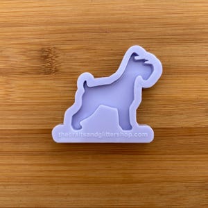 Peut inclure: Un moule en silicone violet en forme de miniature de Schnauzer. Le moule est sur une surface en bois. Thecraftsandglittershop.com est imprimé au bas du moule.