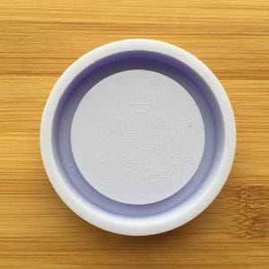 Puede incluir: Un molde redondo de silicona blanco con una hendidura circular en el centro. El molde está diseñado para crear artesanías de resina.