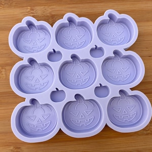 May include: A lavender silicone mould with nine pumpkin-shaped cavities. Each pumpkin has a carved jack-o'-lantern face.