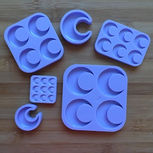 May include: A collection of six light purple silicone moulds featuring various crescent moon shapes. The set includes two square moulds with four large moon cavities, one rectangular mould with six medium moon cavities, one small square mould with nine tiny moon cavities, and two individual crescent moon moulds.
