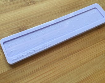 Könnte beinhalten: Eine hellviolette Silikonform in Form eines Lineals mit geprägten Markierungen für Zoll und Zentimeter. Die Form enthält den Text "INCH" und die Website "thecraftsandglittershop.com", die deutlich auf der Oberfläche zu sehen sind.