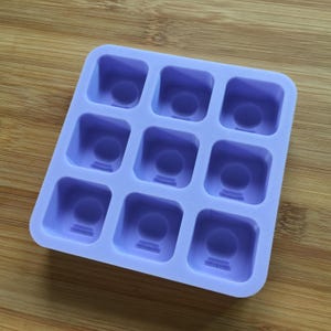 May include: A purple silicone mould with nine square cavities, each with a raised design of a sphere on a base.