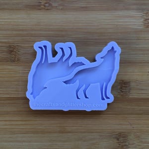 May include: Purple silicone mold of a howling wolf with two smaller wolves behind it. The mold is on a wooden surface. The text "thecraftsandglittershop.com" is at the bottom of the mold.