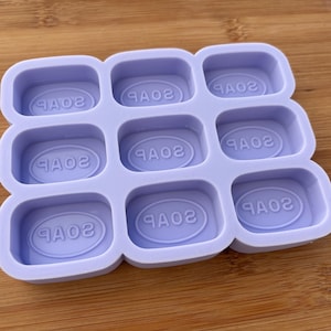 Könnte beinhalten: Eine lilafarbene Silikonform mit neun rechteckigen Vertiefungen, jede mit dem Wort "SOAP" in einer ovalen Form geprägt.