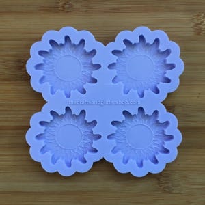 Könnte beinhalten: Eine lilafarbene Silikonform mit vier Sonnenblumen-Designs. Jede Sonnenblume hat eine kreisförmige Mitte und ein detailliertes Blütenblatt-Design.