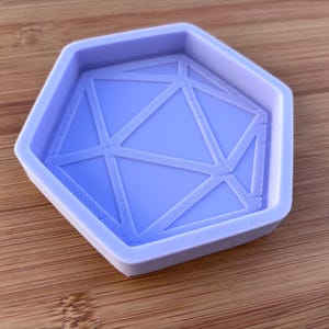 Op de afbeelding: Een lichtpaarse siliconen mal met een geometrisch patroon. De zeshoekige mal heeft een opstaande rand en elkaar kruisende lijnen die een geometrisch ontwerp vormen. Het ligt op een houten oppervlak.