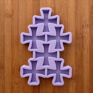 Può includere: Una pila di sei stampi a forma di croce di colore viola chiaro. Gli stampi sono disposti in un motivo verticale, con ogni croce che si incastra con le altre. Lo sfondo è una superficie di legno.