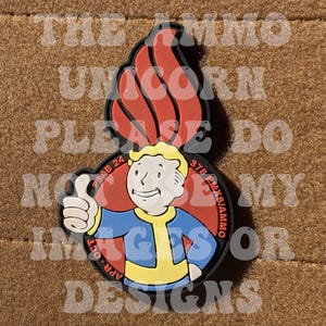 May include: A colorful Fallout-themed design featuring the Vault Boy character giving a thumbs-up. The design includes a red flame, blue and yellow clothing, and text that reads "PSAB 24 APR-OCT 378 EMXS/AMMO".