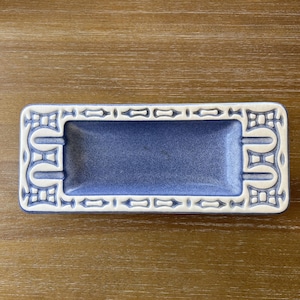 May include: Rectangular ashtray with a speckled blue interior and a white border. The border features a repeating geometric design. The ashtray is made of ceramic or a similar material.