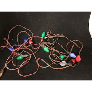 May include: A string of vintage Christmas lights with red, green, and blue bulbs. The lights are connected by red and green wires and have a standard plug. The bulbs are teardrop-shaped.