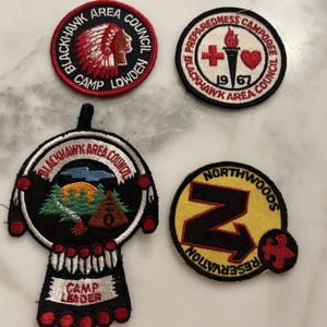 Op de afbeelding: Vier geborduurde patches met verschillende ontwerpen. Eén patch toont een Indiaanse chef, een andere heeft een kruis en een hart, een derde toont een camping en de laatste heeft een grote letter "Z" met een pijl.