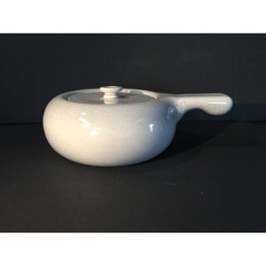 Könnte beinhalten: Eine gesprenkelte, hellgraue Keramik-Suppenschüssel mit Deckel und Griff. Die Schüssel hat eine runde Form und einen kleinen Knopf auf dem Deckel. Der Griff ist gebogen und geht von der Seite der Schüssel aus.