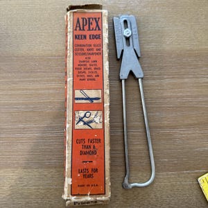 May include: An Apex Keen Edge combination glass cutter, knife, and scissors sharpener. The vintage tool is silver and has a handle. The box is orange and red with text that reads "Cuts faster than a diamond" and "Made in USA."