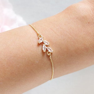 May include: A delicate gold chain bracelet with a small cluster of clear crystal stones in the shape of leaves.