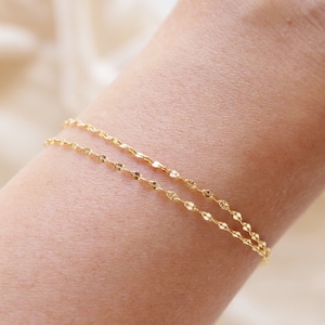 Könnte beinhalten: Ein zartes goldenes Kettenarmband mit strukturierter Oberfläche. Das Armband ist zweimal um ein Handgelenk gelegt.