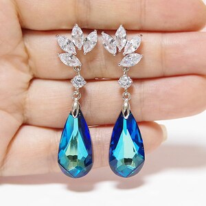Puede incluir: Un par de pendientes colgantes de plata con cristales azules en forma de lágrima y un grupo de piedras de circonita cúbica transparentes en la parte superior.