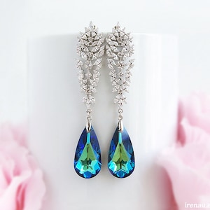 Puede incluir: Un par de pendientes colgantes de plata con un colgante de cristal azul y verde en forma de lágrima. Los pendientes presentan un delicado diseño floral con cristales transparentes.