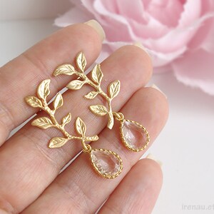 May include: Gold leaf earrings with clear teardrop crystals hanging from the branches. The earrings are delicate and feminine.