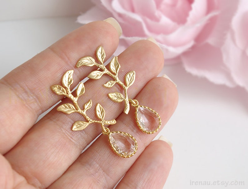May include: Gold leaf earrings with clear teardrop crystals hanging from the branches. The earrings are delicate and feminine.