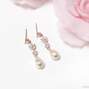 May include: A pair of gold earrings with a pearlescent drop and a delicate crystal design. The earrings are on a white background.