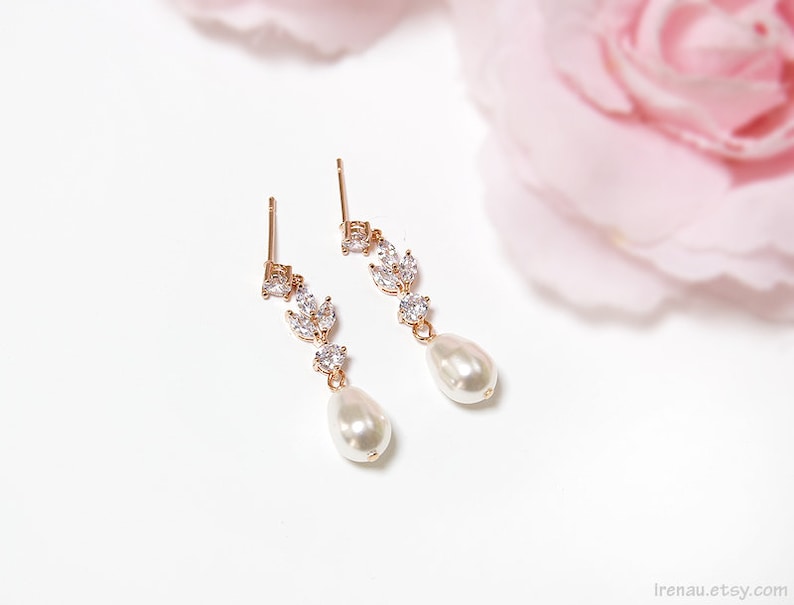 May include: A pair of gold earrings with a pearlescent drop and a delicate crystal design. The earrings are on a white background.