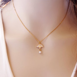 May include: A gold-coloured necklace with a fan-shaped pendant adorned with clear crystals and a small, dangling pearl. The fine chain and pendant design offers a sophisticated aesthetic, suitable for adding a touch of glamour to any ensemble.