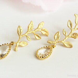 May include: Gold leaf earrings with clear teardrop crystals. The leaves are delicate and detailed, and the crystals are faceted.