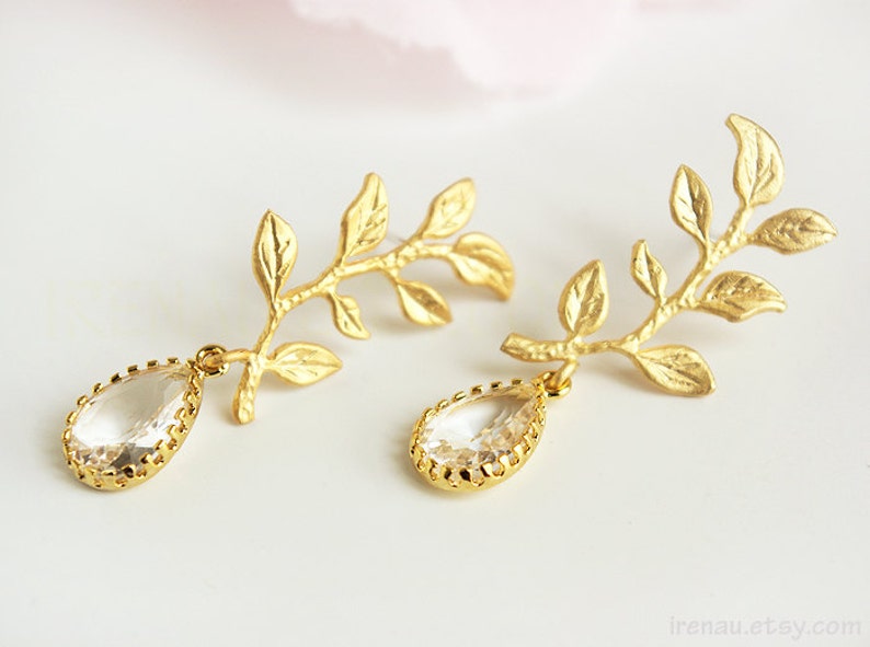 May include: Gold leaf earrings with clear teardrop crystals. The leaves are delicate and detailed, and the crystals are faceted.