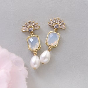 May include: A pair of gold earrings with a white opal-like stone and a pearl dangle. The earrings feature a fan-shaped design with clear rhinestones.