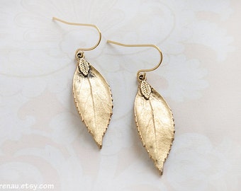 Puede incluir: Pendientes de hoja de oro con un delicado diseño de hoja. Los pendientes están hechos de metal y tienen un acabado dorado.