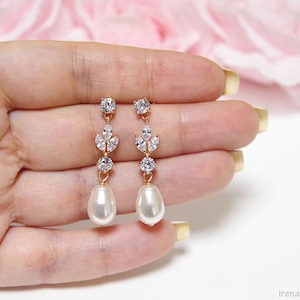 May include: A pair of gold earrings with a pearlescent drop and a crystal leaf design.