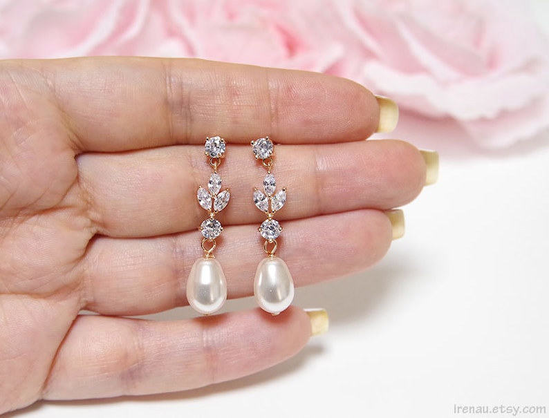 May include: A pair of gold earrings with a pearlescent drop and a crystal leaf design.