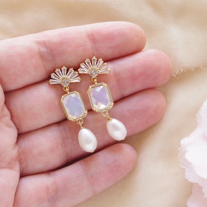 May include: A pair of gold earrings with a clear rectangular stone and a pearl drop. The earrings feature a fan-shaped design with clear rhinestones.