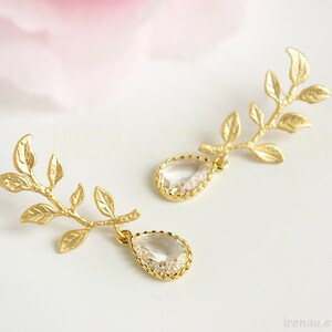 May include: Gold leaf earrings with clear teardrop crystals. The earrings feature a delicate branch design with multiple leaves.