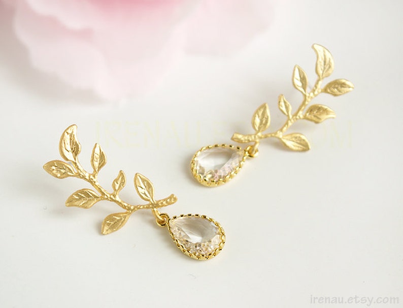 May include: Gold leaf earrings with clear teardrop crystals. The earrings feature a delicate branch design with multiple leaves.