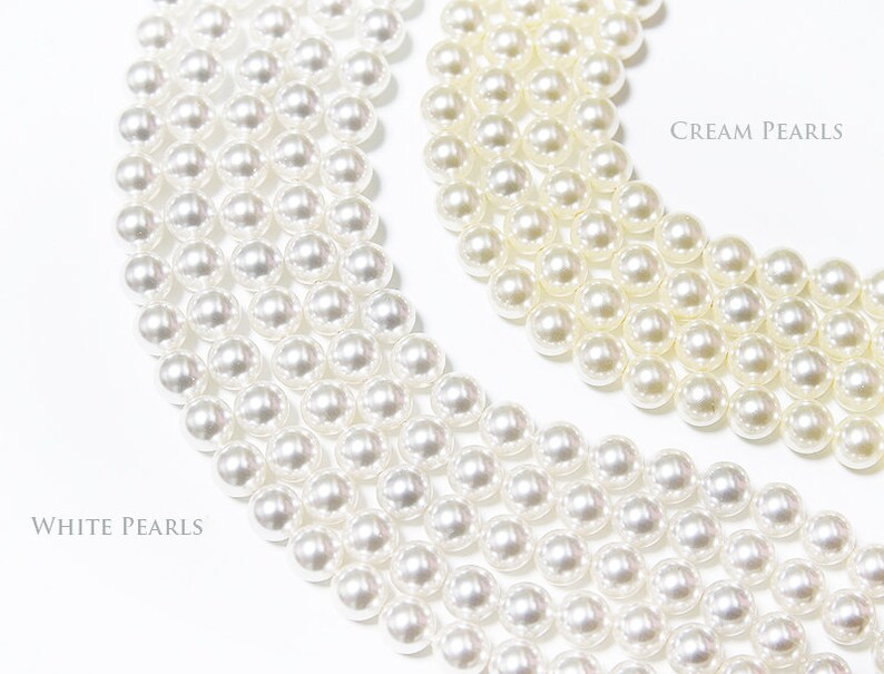 May include: Close-up of white and cream-coloured pearl strands. The image shows multiple strands of pearls, with the text "White Pearls" and "Cream Pearls" labelling the different colours. The pearls are round and have a glossy finish.