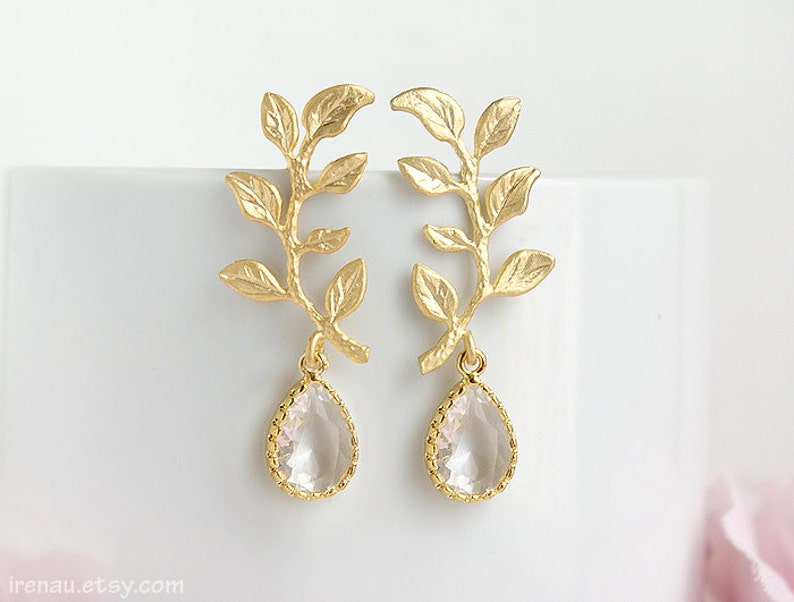 May include: Gold leaf earrings with a teardrop shaped clear crystal hanging from each branch. The earrings are delicate and feminine.