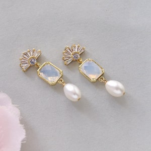 May include: A pair of gold earrings with a white opal-like stone and a pearl drop. The earrings feature a fan-shaped design with clear rhinestones.