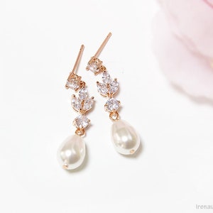 May include: A pair of gold earrings with a pearlescent drop and a cluster of clear cubic zirconia stones in a leaf design.