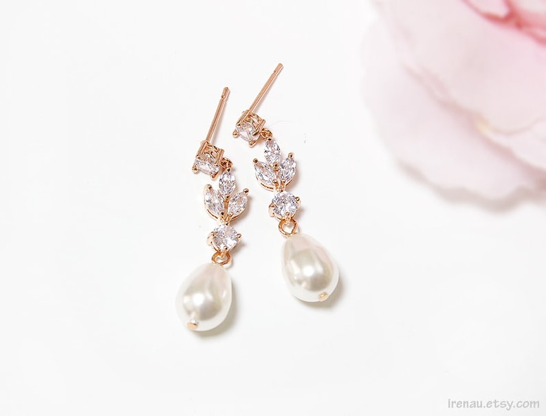 May include: A pair of gold earrings with a pearlescent drop and a cluster of clear cubic zirconia stones in a leaf design.