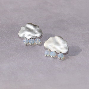 Può includere: Un paio di orecchini a forma di nuvola argentati con gocce di pioggia di opale che pendono dalla parte inferiore.