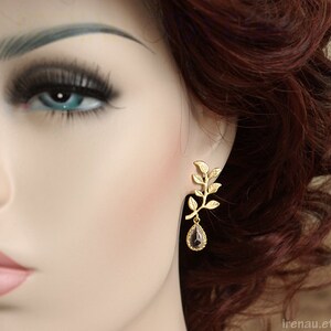 May include: Gold leaf earrings with a dangling teardrop-shaped gemstone. The gemstone is a dark purple color.
