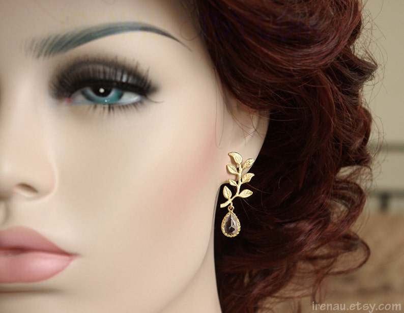 May include: Gold leaf earrings with a dangling teardrop-shaped gemstone. The gemstone is a dark purple color.