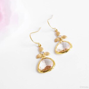以下が含まれることがあります： クリアな涙型のクリスタルと繊細な花のアクセントが付いた、ゴールドのイヤリングのペアです。