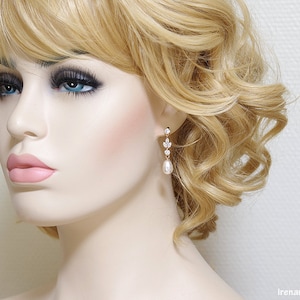 May include: Gold dangle earrings with a pearlescent drop and crystal accents. The earrings are shown on a model with blonde hair.