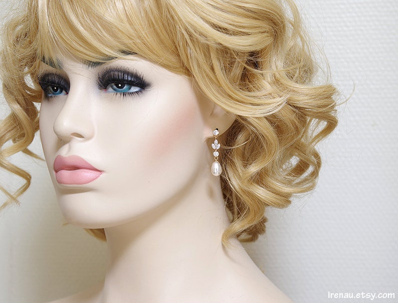 May include: Gold dangle earrings with a pearlescent drop and crystal accents. The earrings are shown on a model with blonde hair.