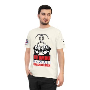Könnte beinhalten: Ein weißes T-Shirt mit einer schwarz-weißen Grafik von zwei Fäusten, die einen Haken halten. Der Text "HO'OMAU HAWAII LONGSHOREMEN" ist in Rot und Blau unter der Grafik gedruckt.