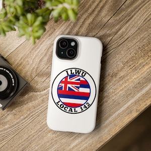 Könnte beinhalten: Weiße iPhone-Hülle mit einem schwarzen Kreis, der den Text "ILWU LOCAL 142" und eine hawaiianische Flagge enthält.