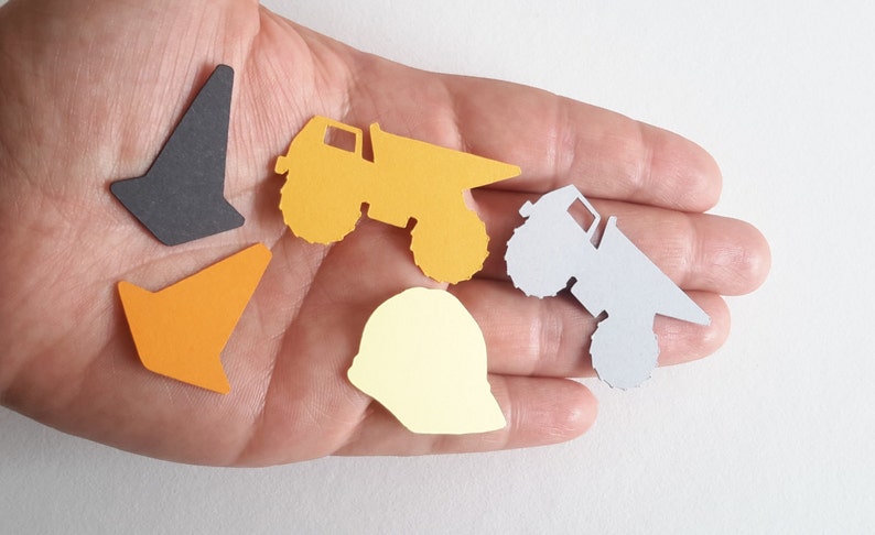 May include: A set of five paper cutouts in the shape of construction vehicles and a hard hat. The cutouts are yellow, orange, grey, and black.