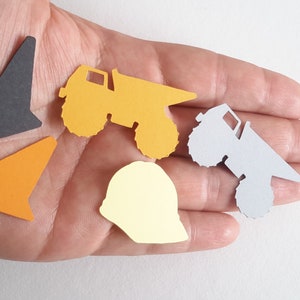 May include: Five paper cut-outs of construction vehicles and a hard hat. The cut-outs are yellow, orange, grey, and black. The hard hat is yellow.